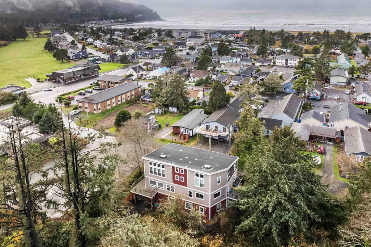 An exterior shot of the house perched on a gentle hill, with a panoramic view of the surrounding neighborhood and the nearby coastline visible. The scene captures a peaceful residential vibe with coastal adventure close at hand.