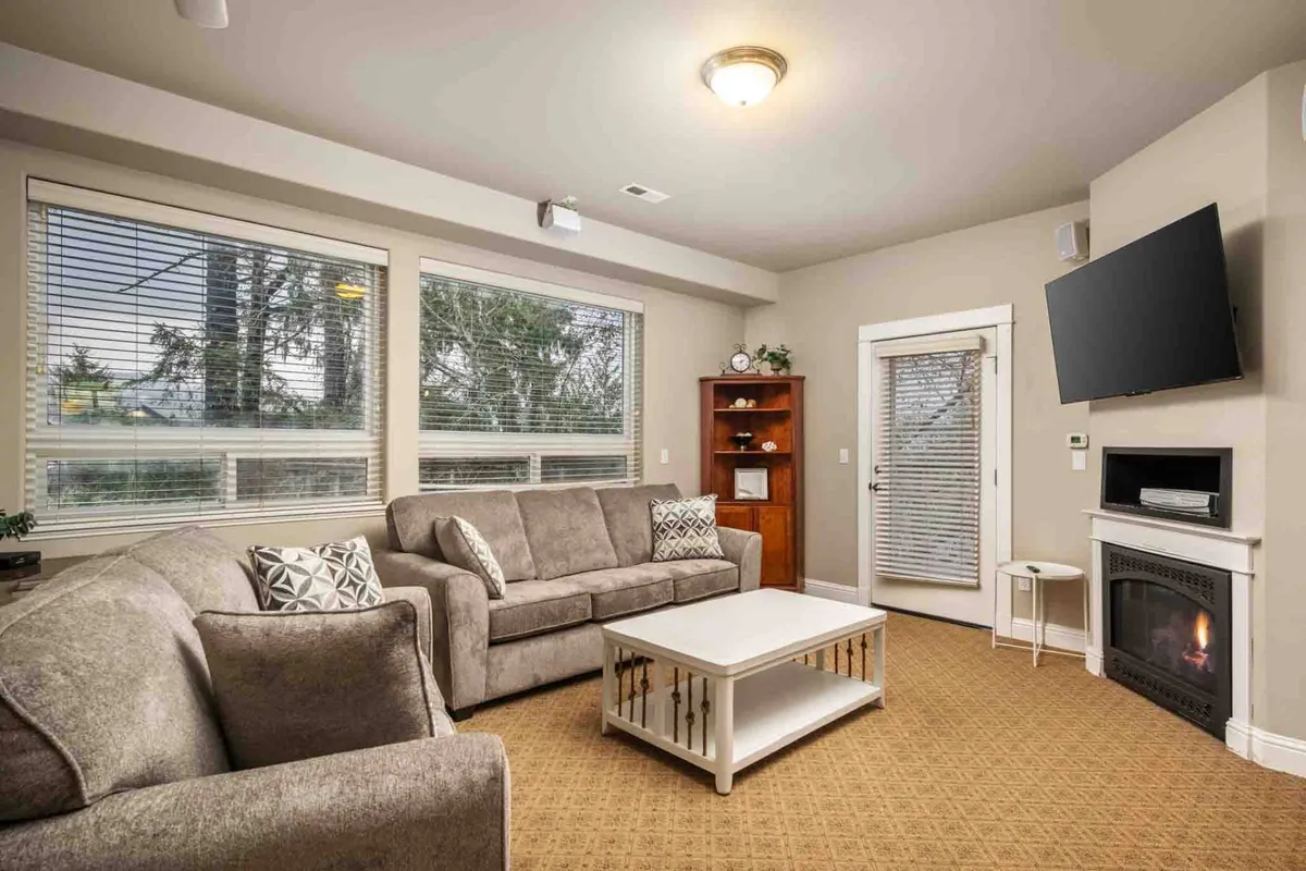 A comfortable, welcoming living space featuring a large, plush sofa, a coffee table, and a fireplace as a focal point. Generous windows let in sunlight, highlighting the warmth and social feel of the area—ideal for cozy evenings, socializing, or family game nights.