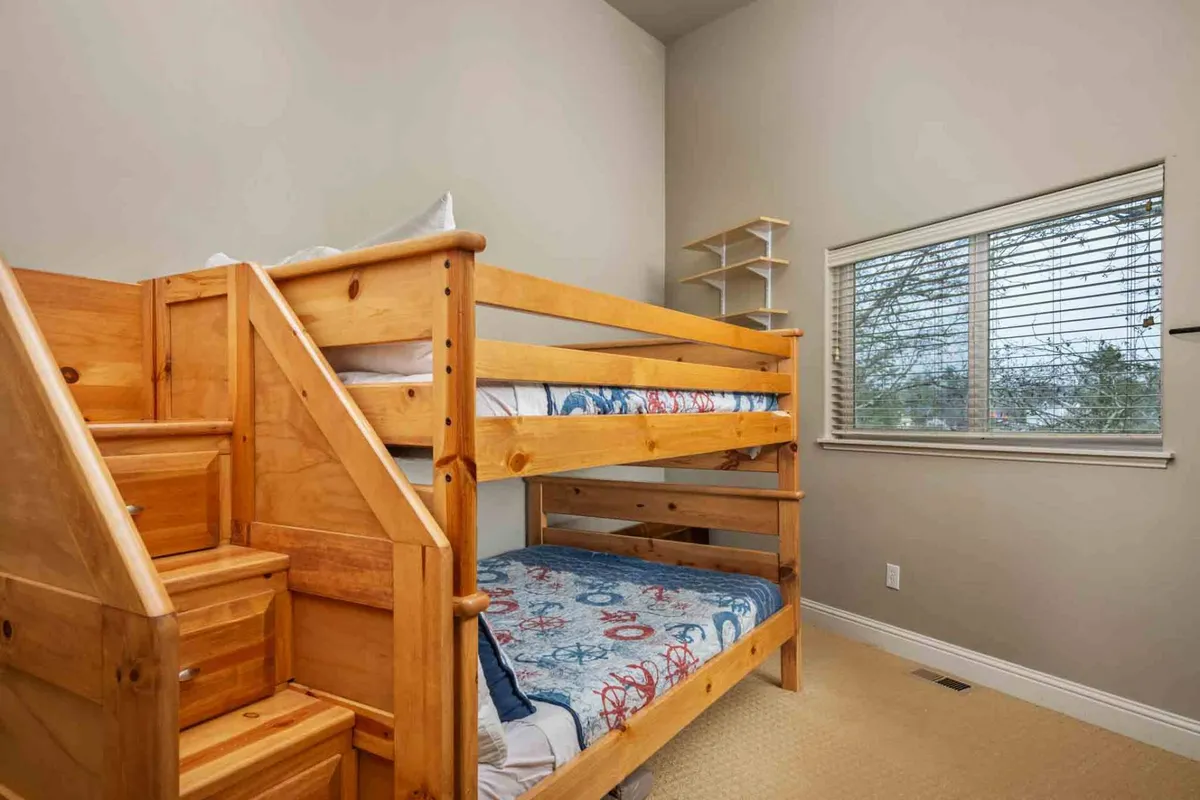 A playful bunk room with a sturdy bunk bed, window with soft natural light, and built-in shelves filled with books and toys. The space is cheerful and inviting for children, perfect for sleep and play.
