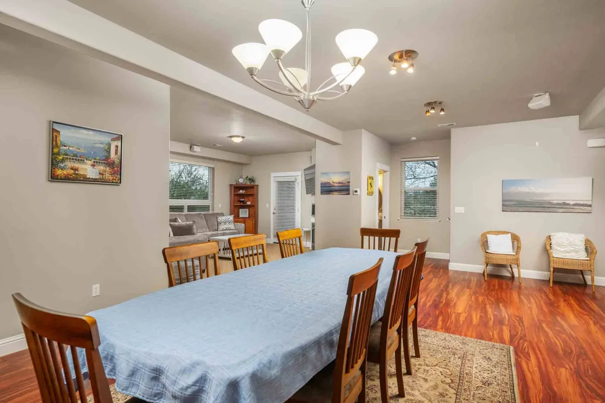 A spacious dining area featuring a large table beneath an elegant chandelier, surrounded by art-adorned walls. The space feels open and ready for memorable family dinners, celebrations, or casual conversations.