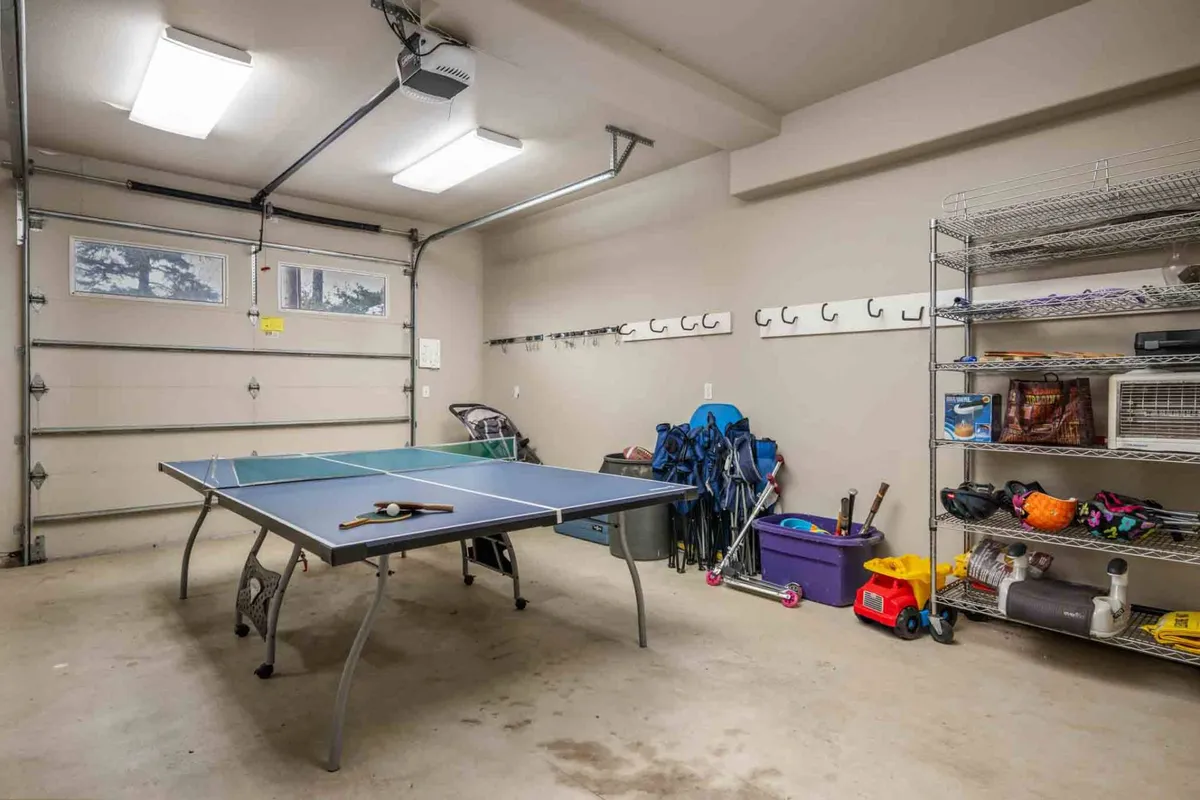 A recreational space showcasing a ping pong table, organized shelves, and a garage door, emphasizing an active, social atmosphere. The area looks spacious and well-lit, perfect for friendly competitions and group gatherings.