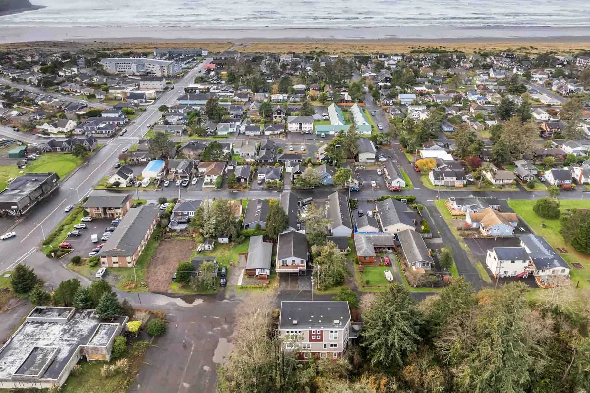 A broad neighborhood view featuring residential homes, the nearby coastline, roadways, and green spaces. The scene suggests proximity to local attractions, easy beach access, and a welcoming community atmosphere.