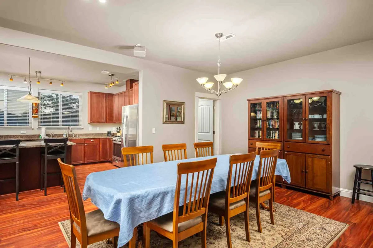 The image highlights a spacious dining area with a large wooden table and matching chairs, complemented by a stylish hutch with glass doors. The set-up invites family dinners, festive celebrations, or lively conversations with friends.