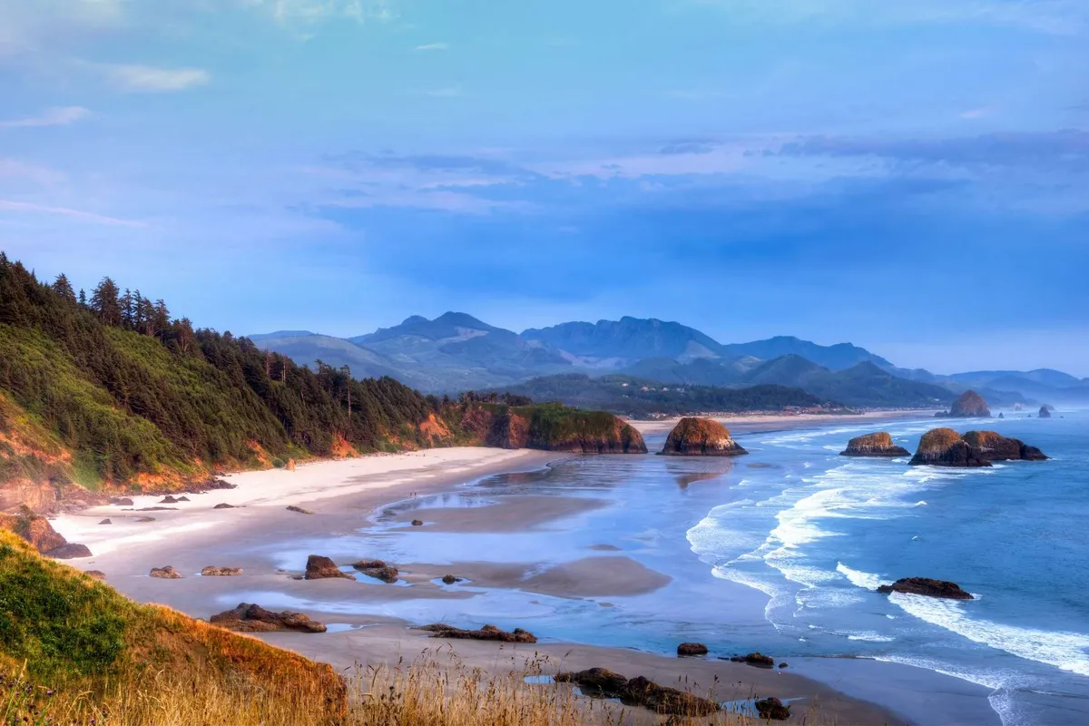 A serene stretch of beach bordered by rocky outcrops and mountains, with the ocean stretching to the horizon. The area is tranquil and inviting, ideal for picnics, birdwatching, and connecting with nature.